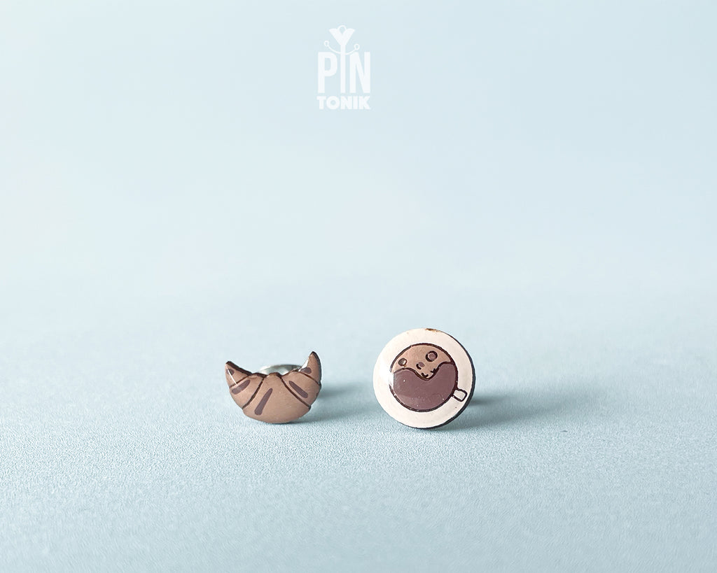 Mismatched hand-painted wooden stud earrings featuring a tiny croissant and a coffee cup with a heart in the foam