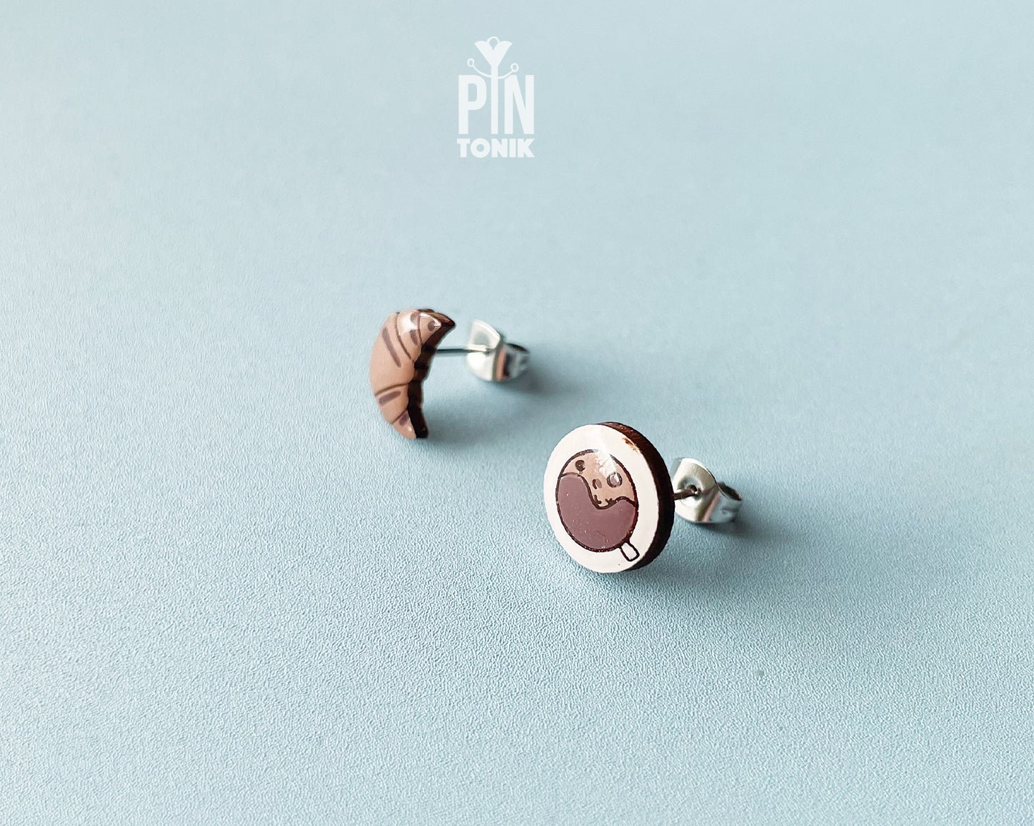 Mismatched hand-painted wooden stud earrings featuring a tiny croissant and a coffee cup with a heart in the foam