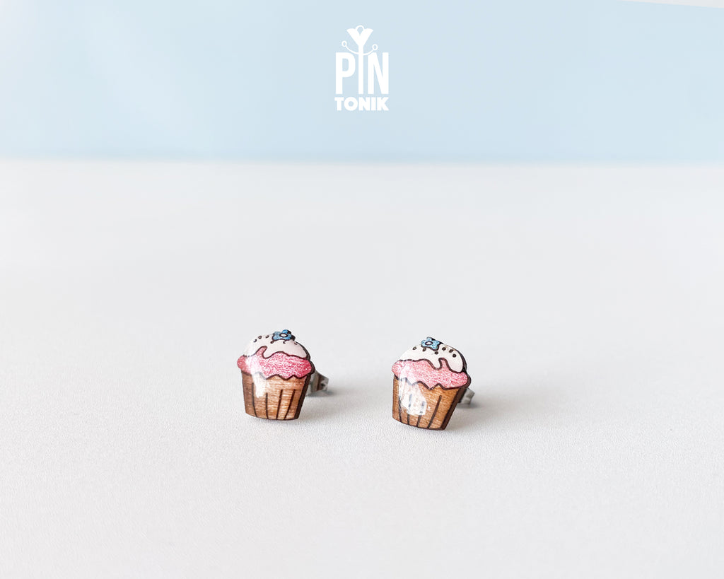 Handmade wooden pink cupcake stud earrings with a brown wrapper and a tiny blue flower sprinkle on top by PinTonik