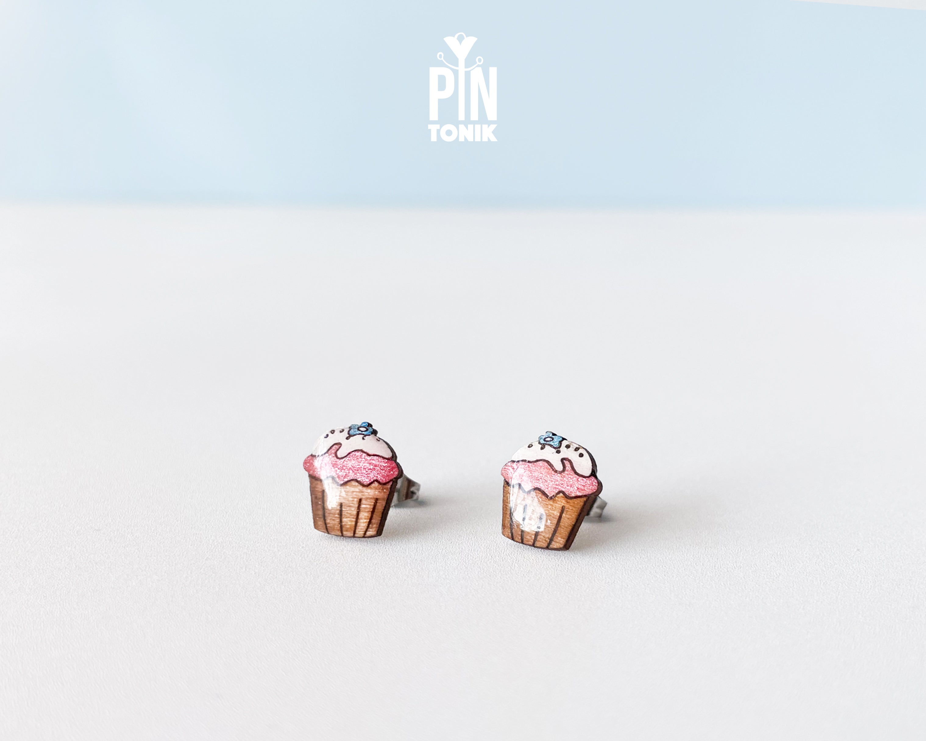 Handmade wooden pink cupcake stud earrings with a brown wrapper and a tiny blue flower sprinkle on top by PinTonik