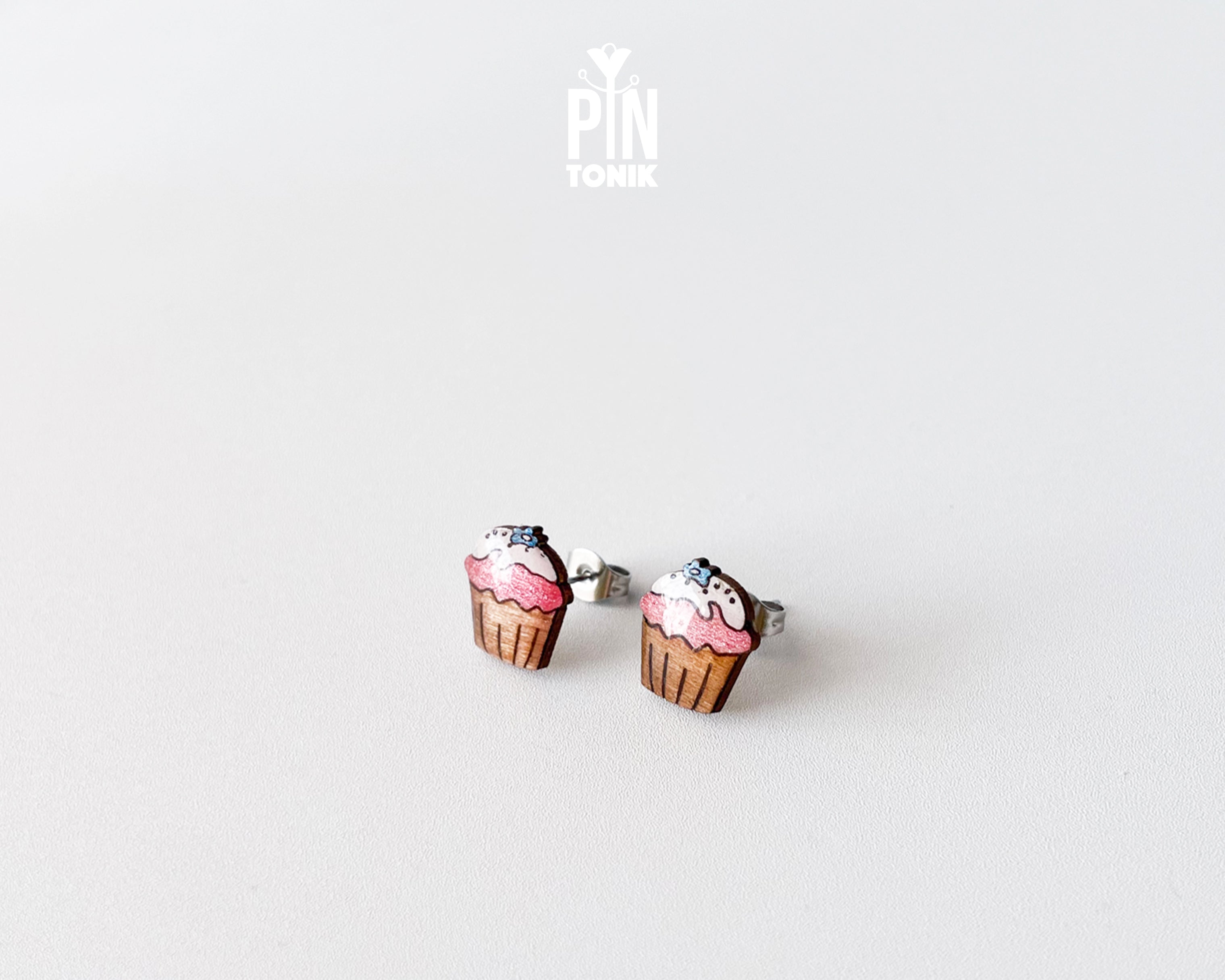 Handmade wooden pink cupcake stud earrings with a brown wrapper and a tiny blue flower sprinkle on top by PinTonik