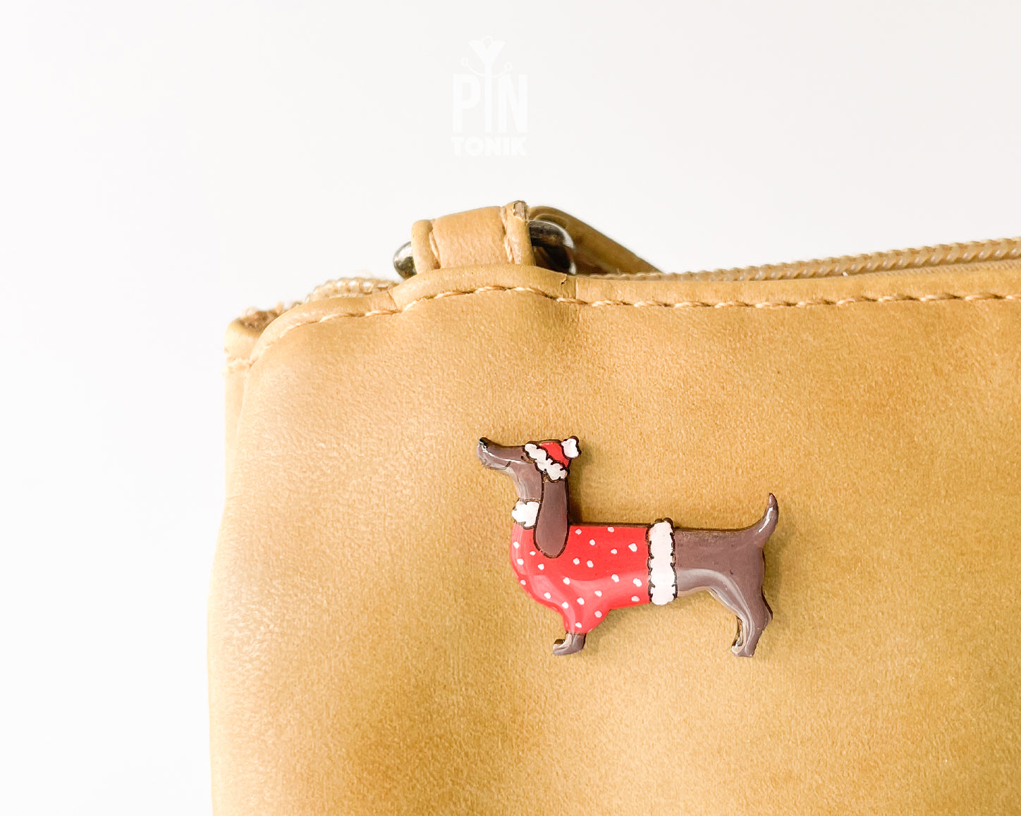 Hand-painted wooden dachshund pin wearing a red Christmas sweater and Santa hat with a glossy resin finish