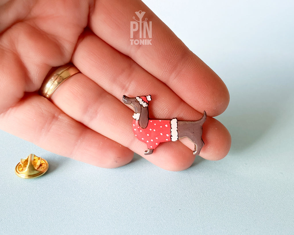 Hand-painted wooden dachshund pin wearing a red Christmas sweater and Santa hat with a glossy resin finish