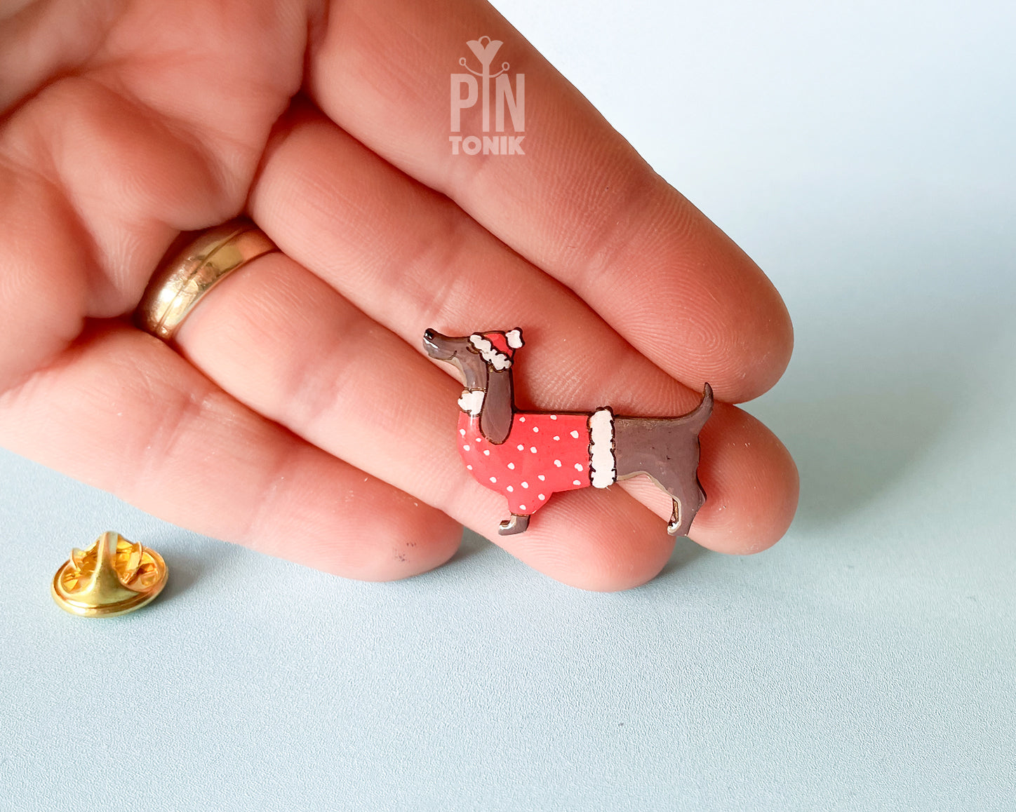 Hand-painted wooden dachshund pin wearing a red Christmas sweater and Santa hat with a glossy resin finish