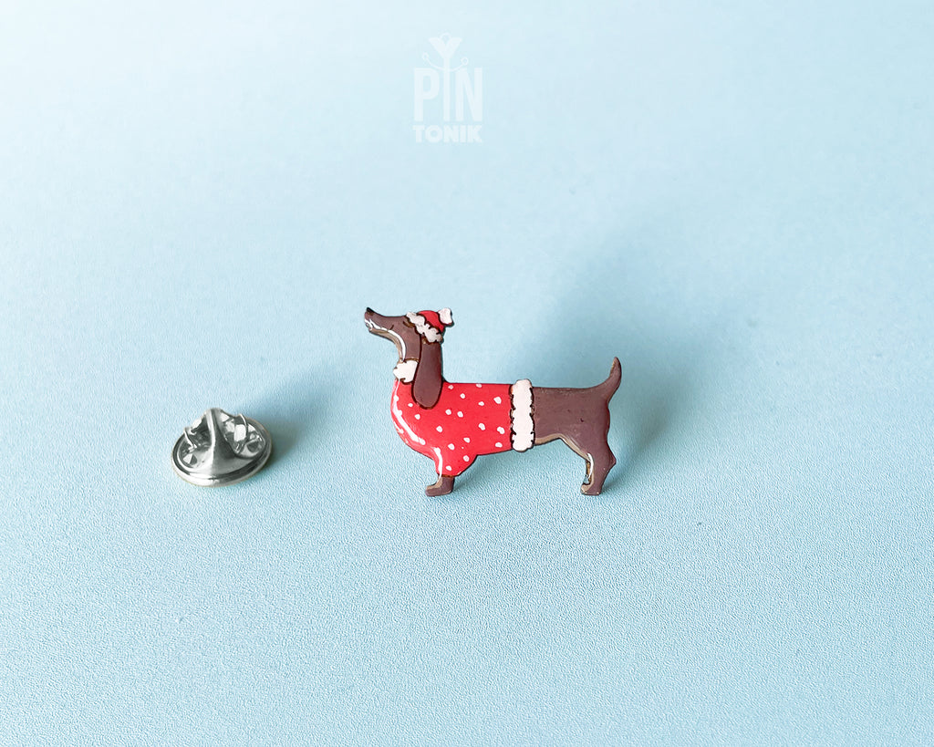 Hand-painted wooden dachshund pin wearing a red Christmas sweater and Santa hat with a glossy resin finish