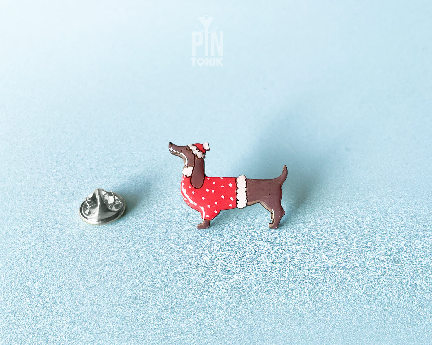 Hand-painted wooden dachshund pin wearing a red Christmas sweater and Santa hat with a glossy resin finish