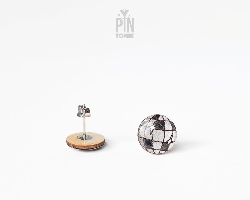 A pair of stud earrings on a clean white background. One earring is shown from the back with a steel post and a round light wood base, while the other is shown from the front with a silver mosaic tile pattern.