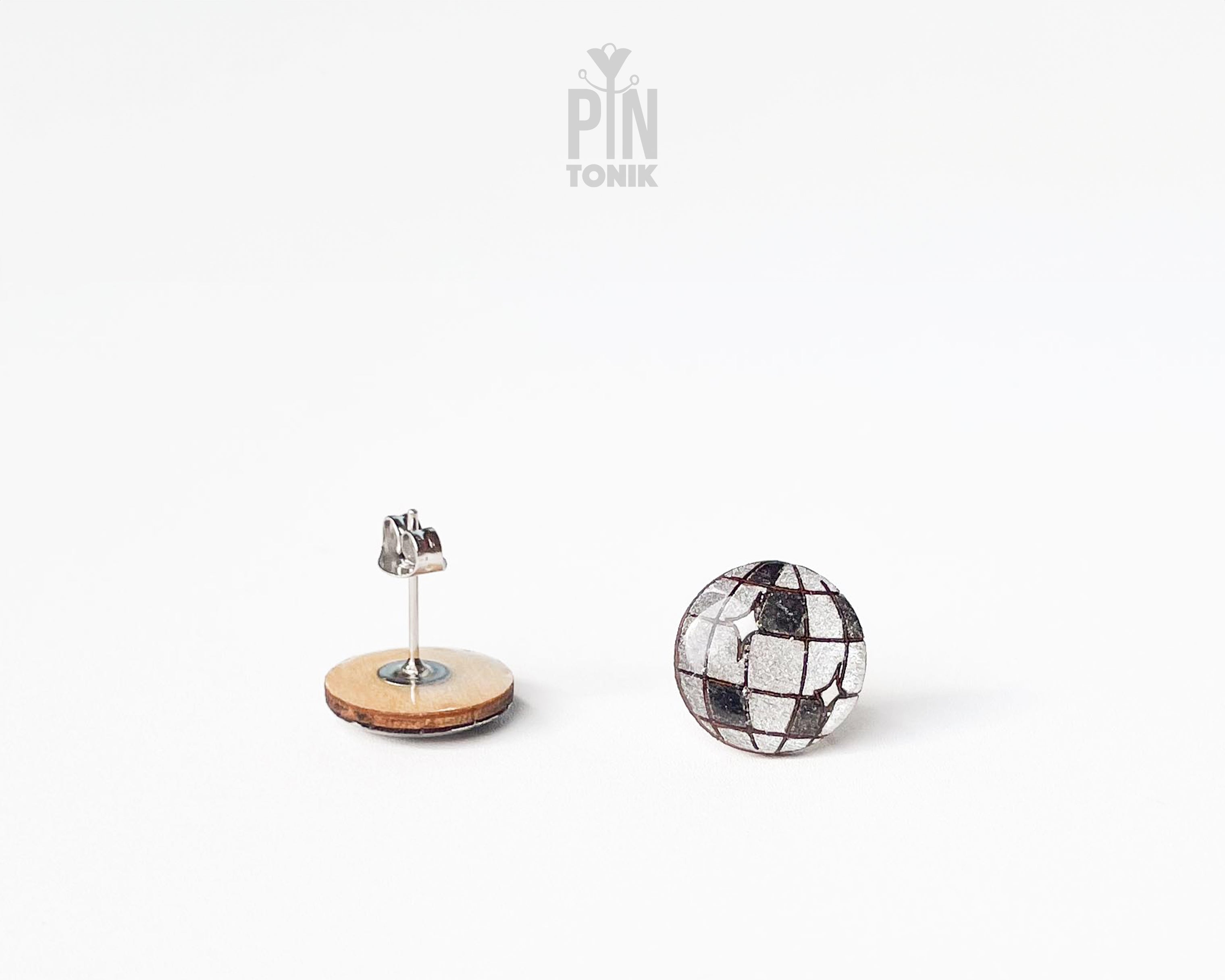 A pair of stud earrings on a clean white background. One earring is shown from the back with a steel post and a round light wood base, while the other is shown from the front with a silver mosaic tile pattern.