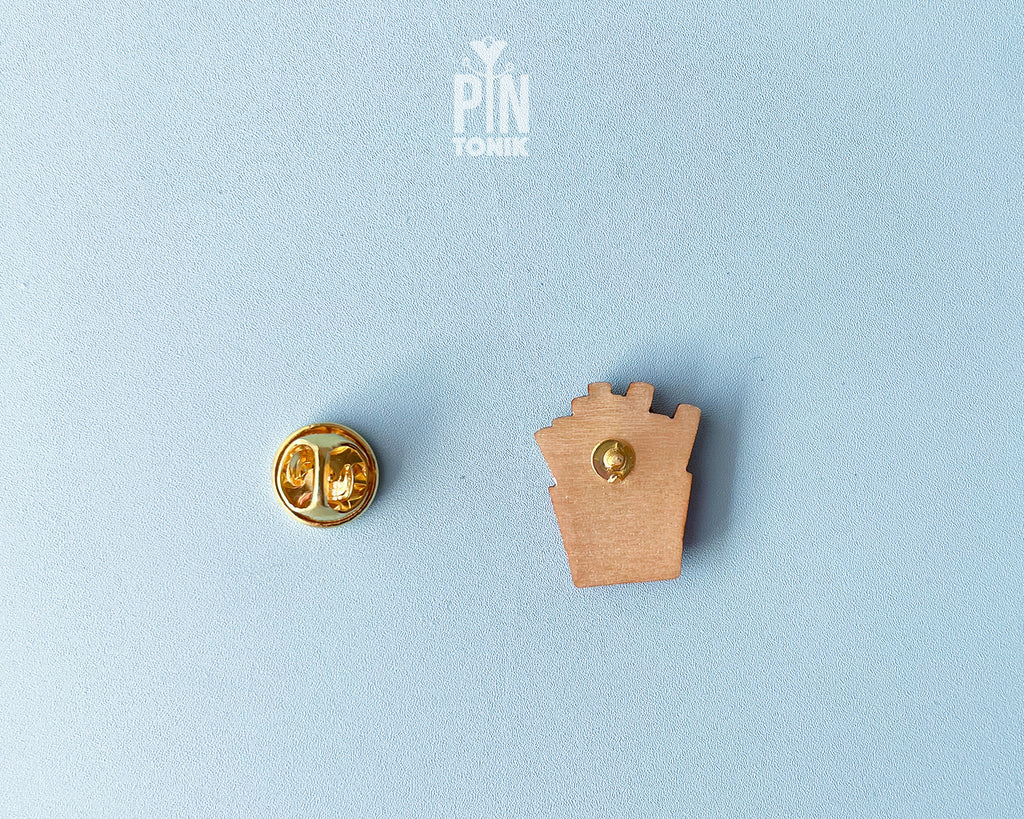 Hand-painted wooden french fries pin in a red carton with a small pink heart, shown next to a stainless steel clutch back on a light blue background.