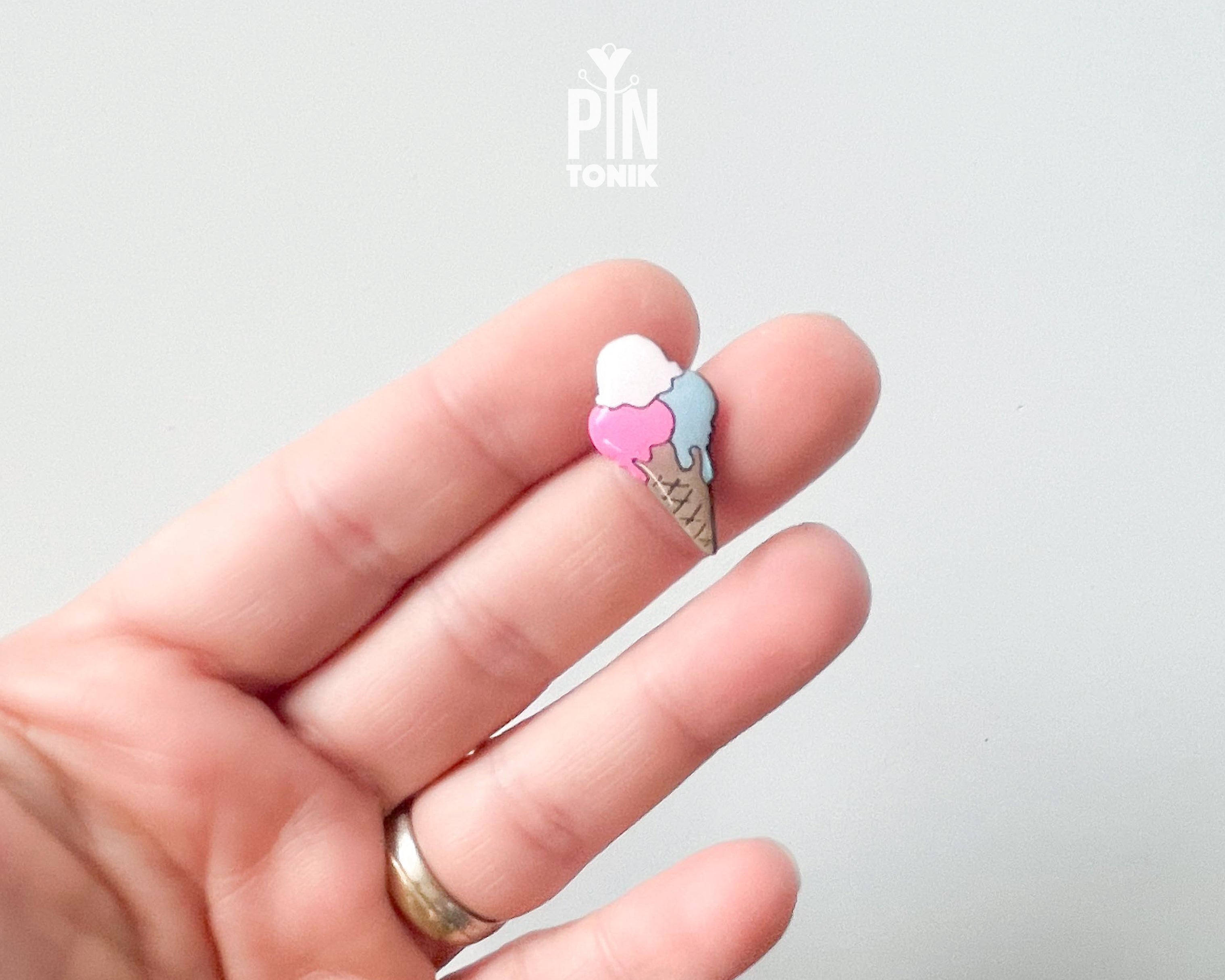 Hand-painted wooden gelato pin with three colorful scoops (pink, white, and blue) on a tan waffle cone, shown pinned to a leather bag