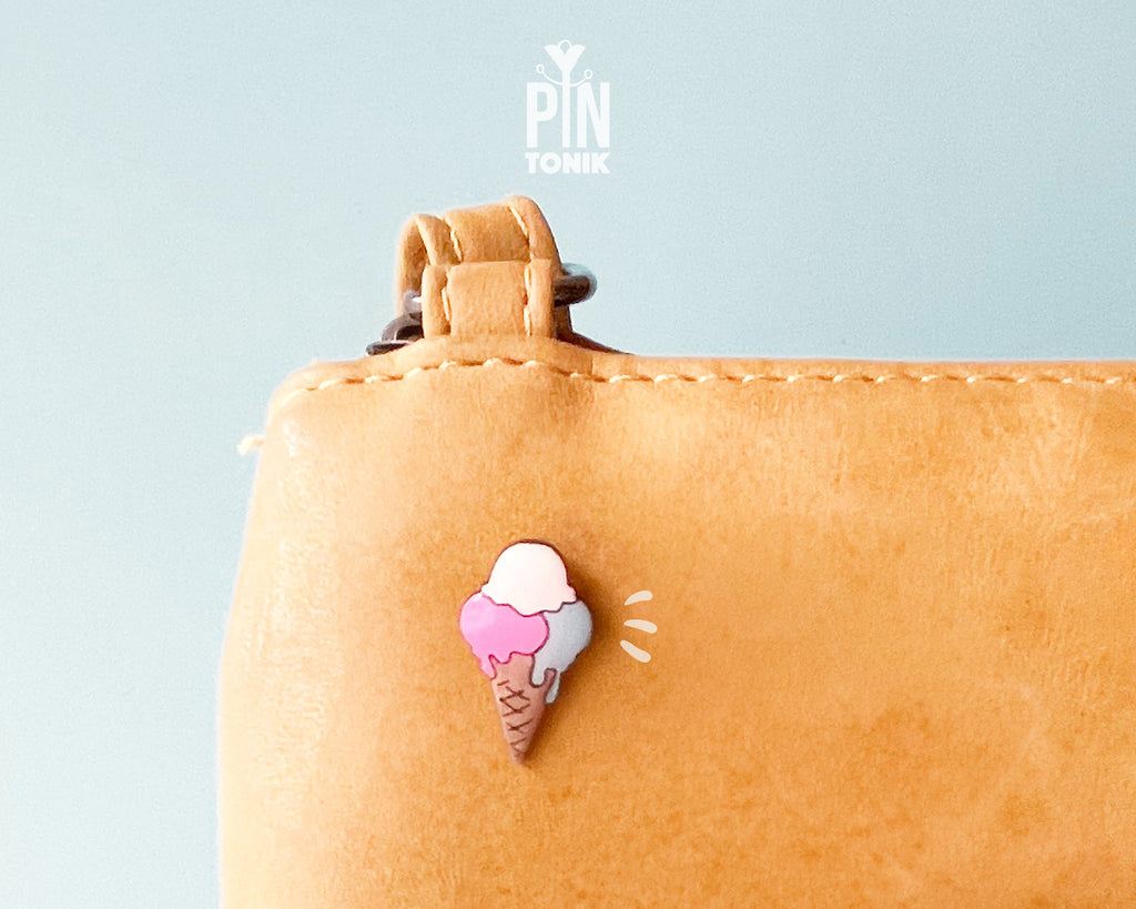 Hand-painted wooden gelato pin with three colorful scoops (pink, white, and blue) on a tan waffle cone, shown pinned to a leather bag