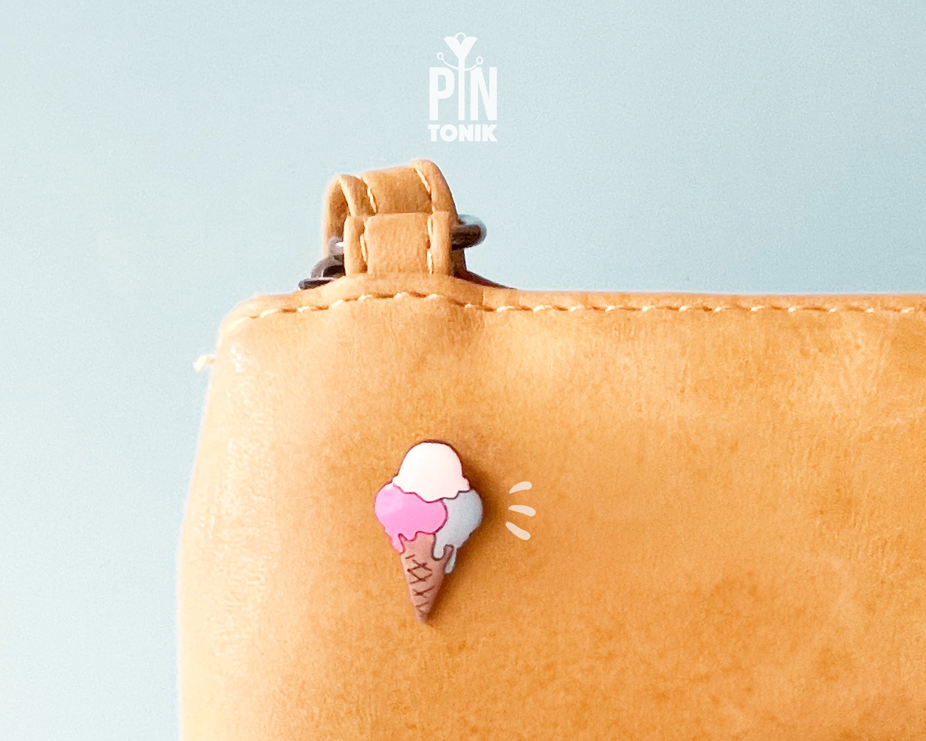 Hand-painted wooden gelato pin with three colorful scoops (pink, white, and blue) on a tan waffle cone, shown pinned to a leather bag