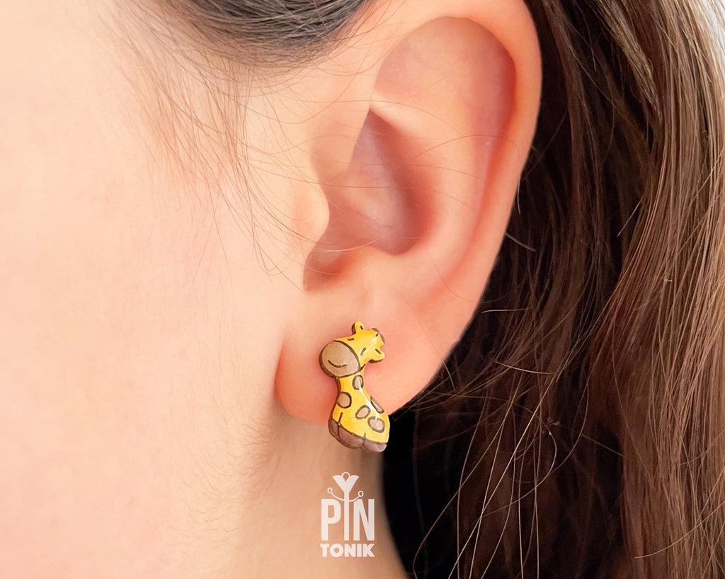 Pair of hand-painted wooden giraffe stud earrings with a glossy resin finish and sleepy expressions