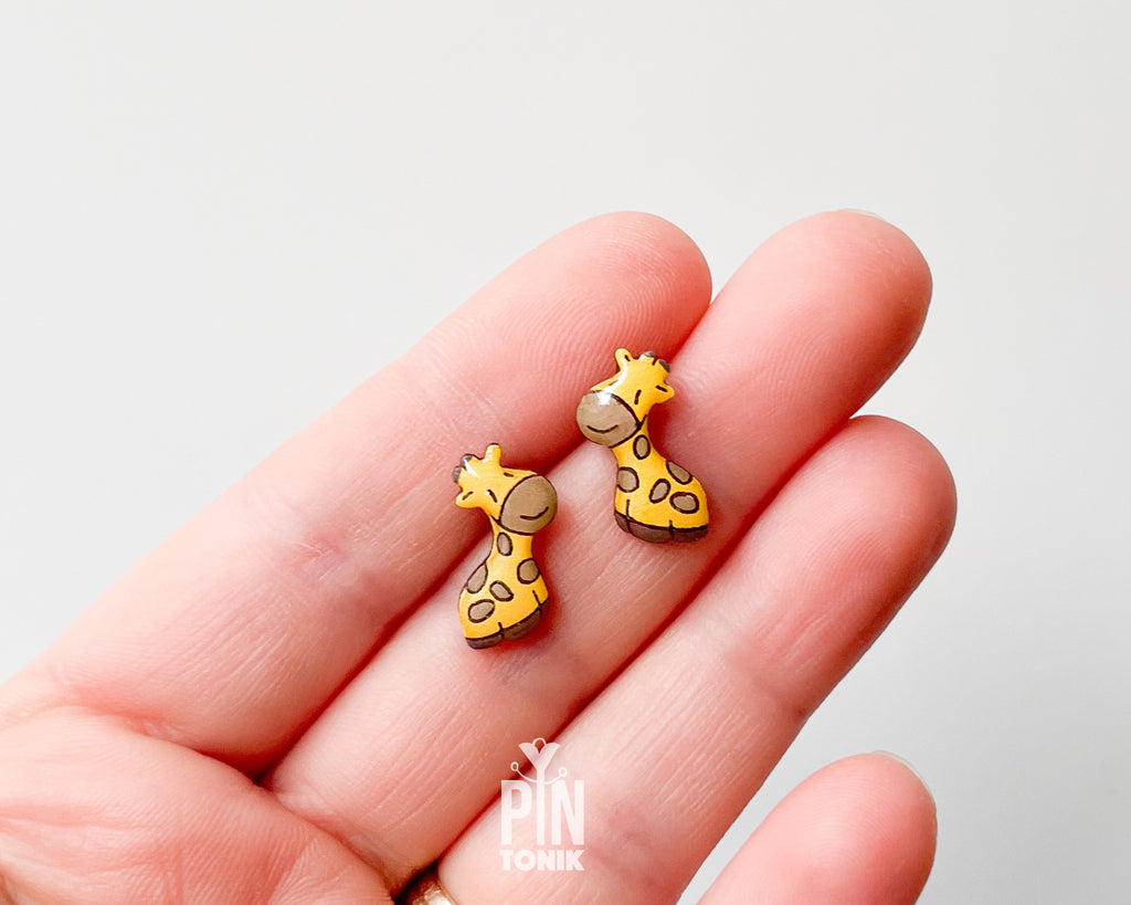 Pair of hand-painted wooden giraffe stud earrings with a glossy resin finish and sleepy expressions