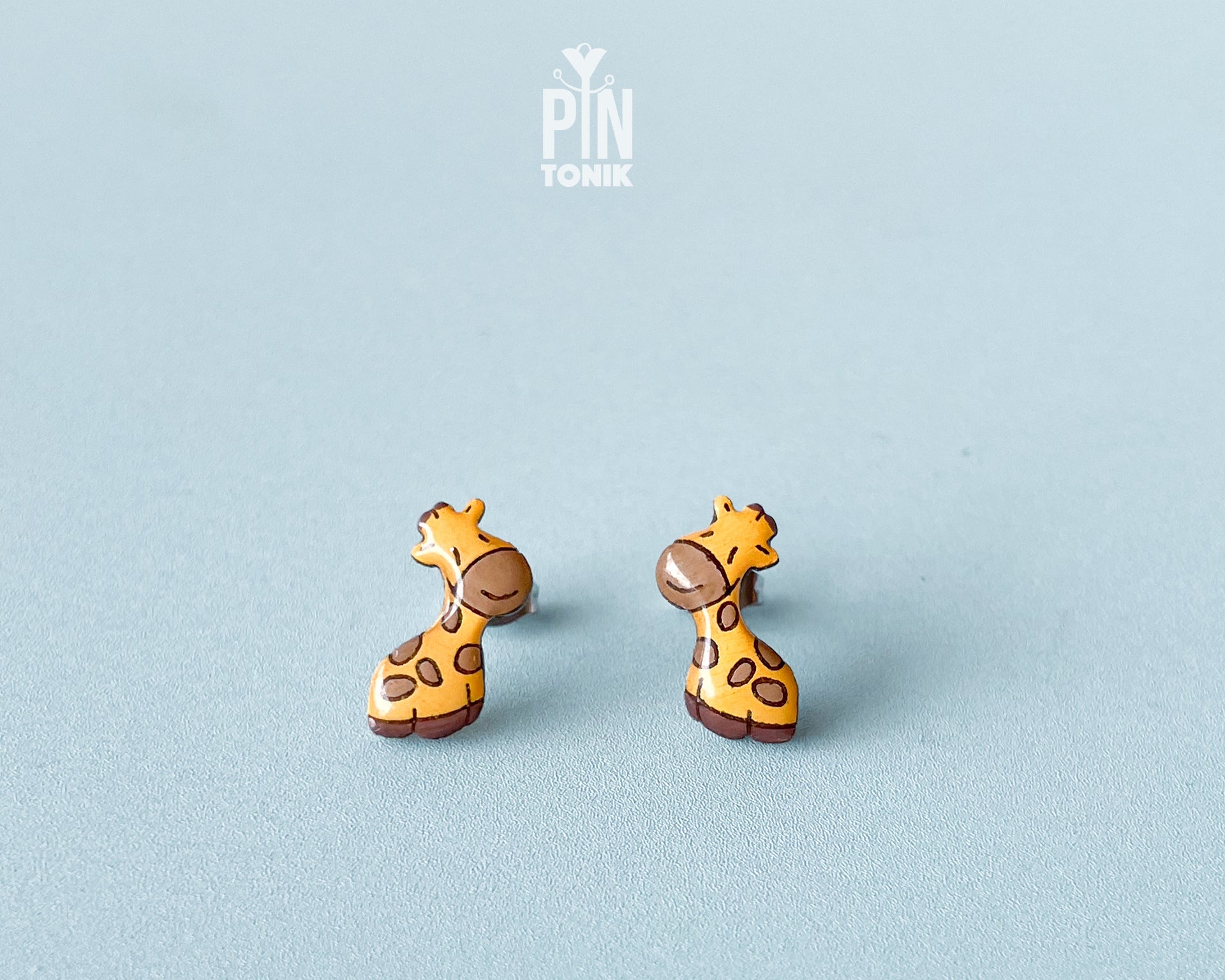 Pair of hand-painted wooden giraffe stud earrings with a glossy resin finish and sleepy expressions
