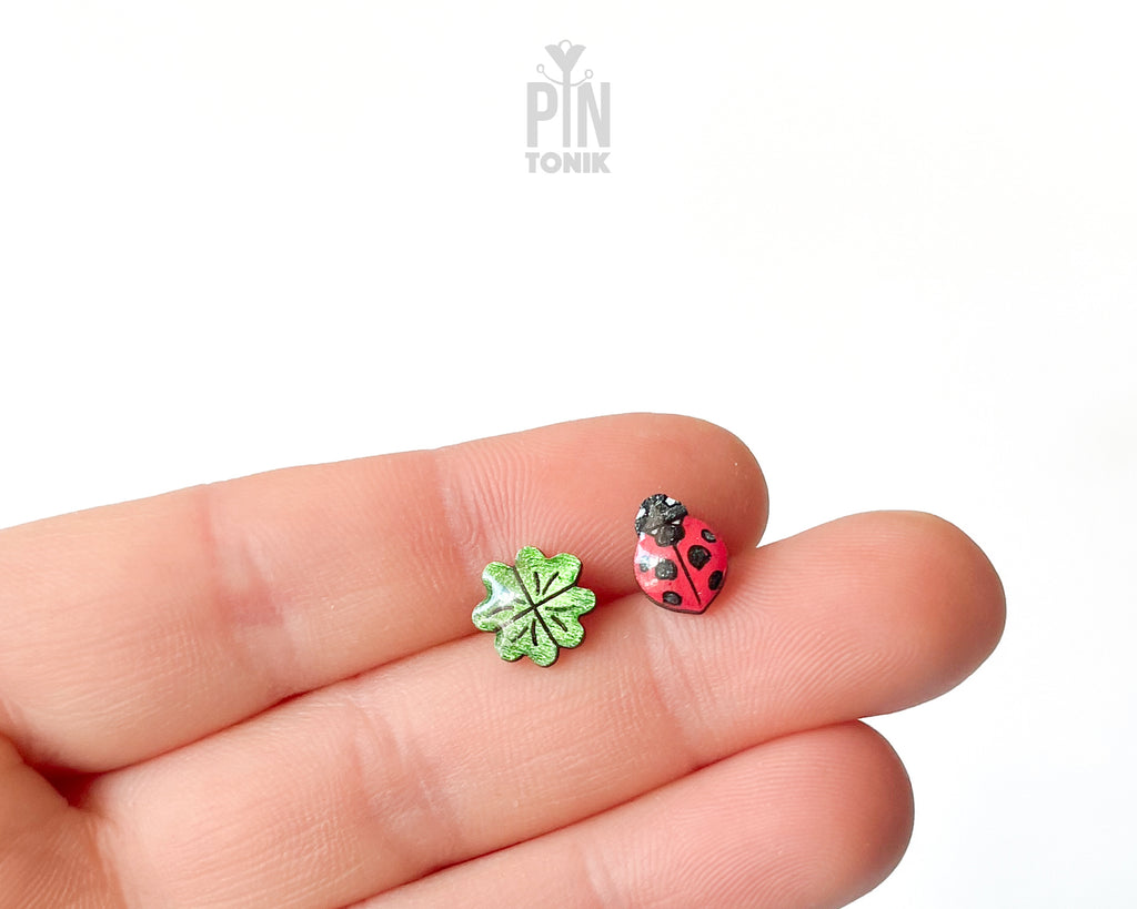 Handmade wooden stud earrings featuring a tiny red ladybug sitting on a green four-leaf clover by PinTonik.
