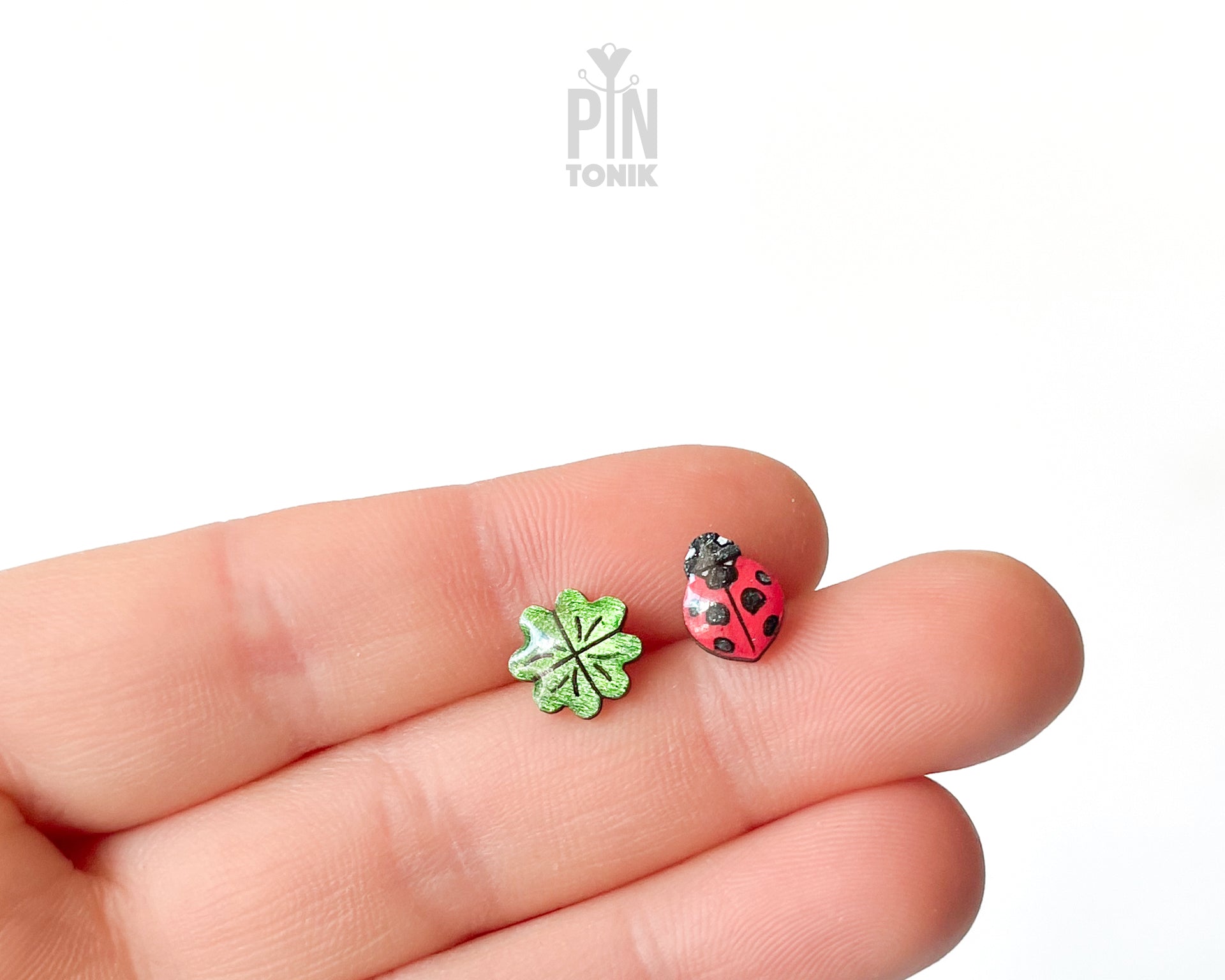 Handmade wooden stud earrings featuring a tiny red ladybug sitting on a green four-leaf clover by PinTonik.