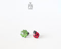Handmade wooden stud earrings featuring a tiny red ladybug sitting on a green four-leaf clover by PinTonik.