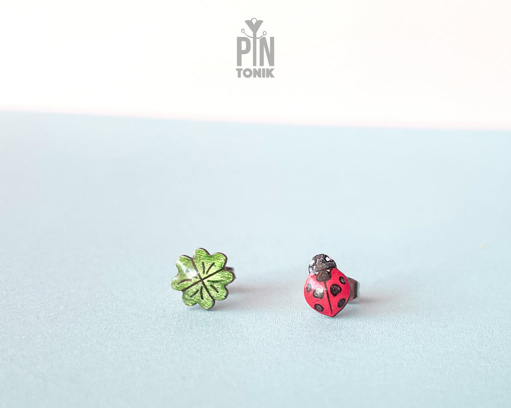 Handmade wooden stud earrings featuring a tiny red ladybug sitting on a green four-leaf clover by PinTonik.