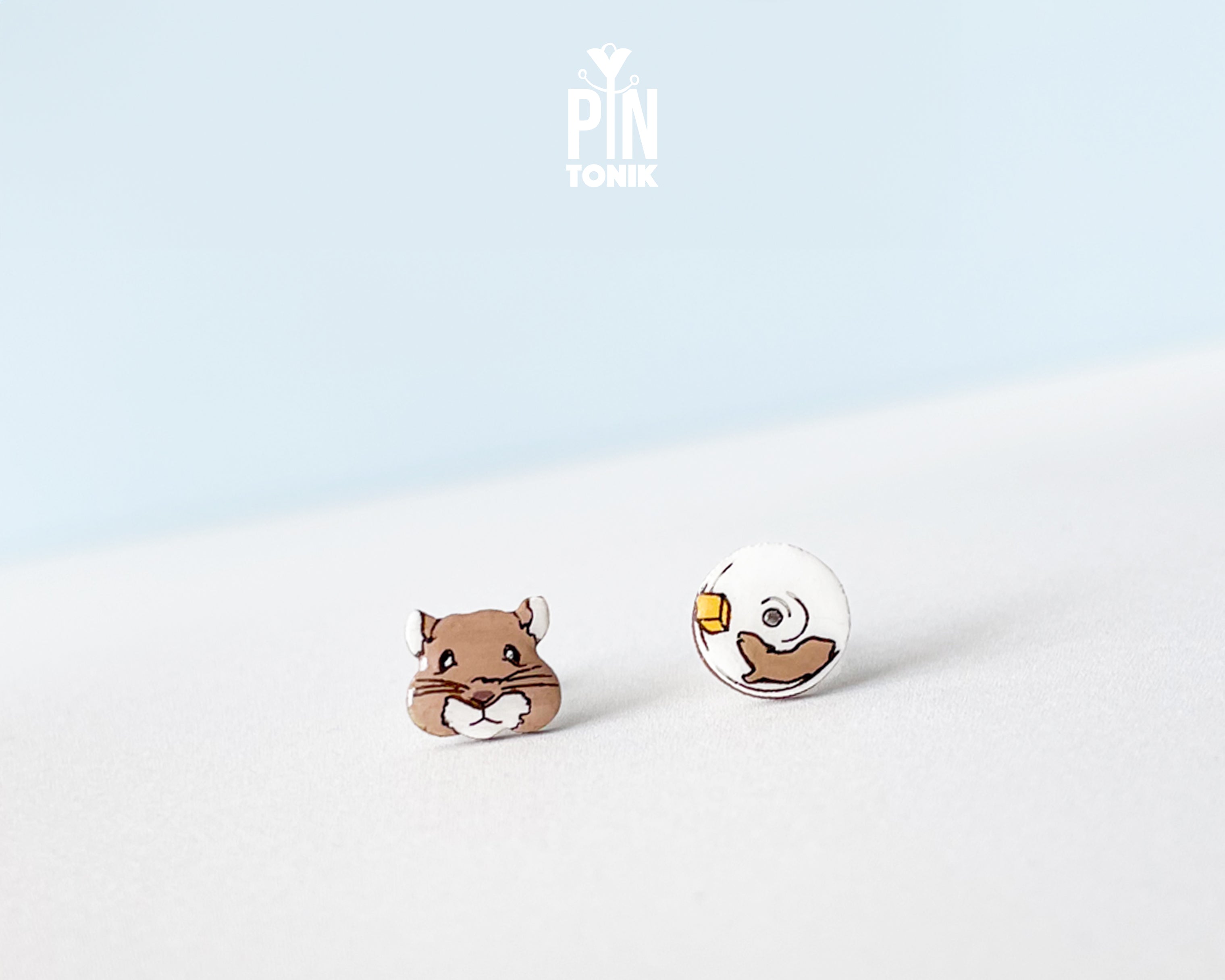 Mismatched hand-painted wooden stud earrings featuring a brown hamster face and a white exercise wheel