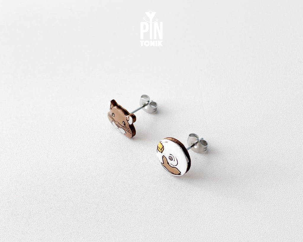 Mismatched hand-painted wooden stud earrings featuring a brown hamster face and a white exercise wheel