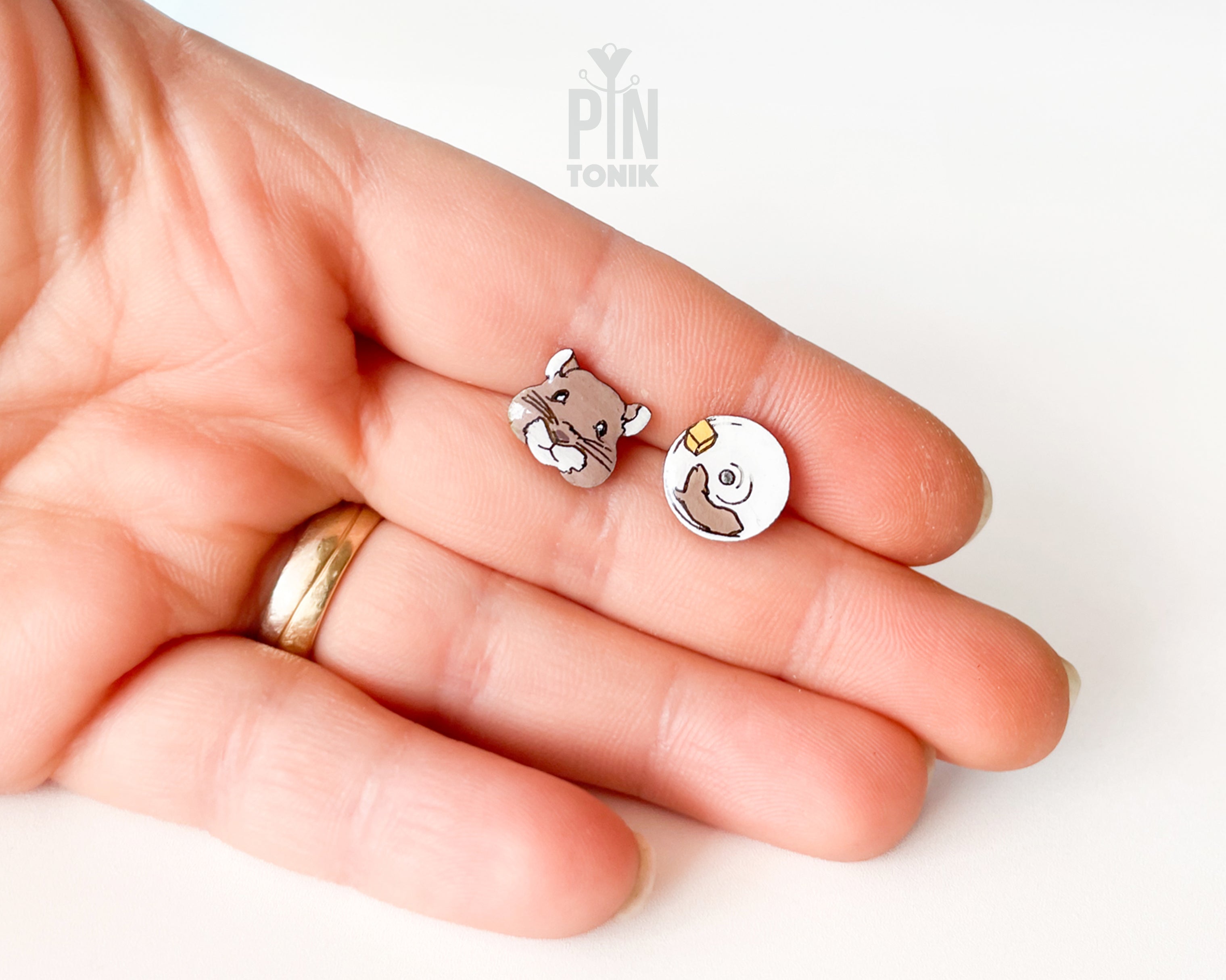 Mismatched hand-painted wooden stud earrings featuring a brown hamster face and a white exercise wheel