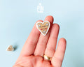Hand-painted wooden gingerbread heart pins with white "icing" edges and floral details. One version features the Tyrolean text "I mag Di" while the other is a simple floral heart.