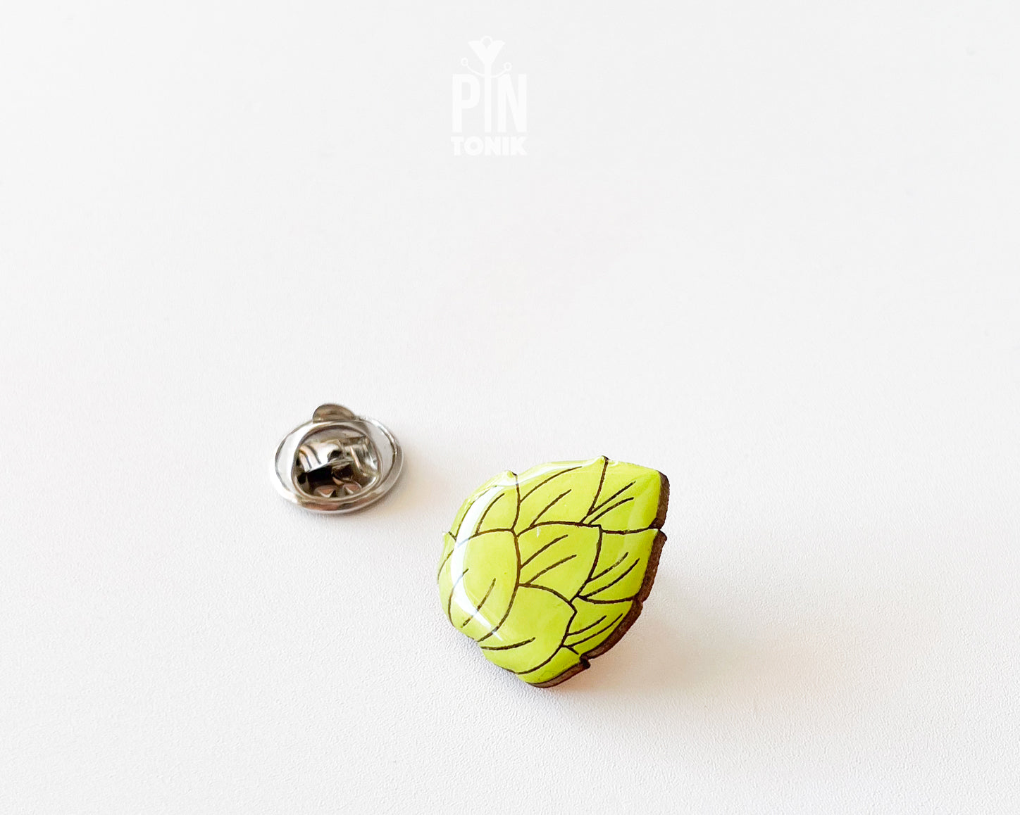 Hand-painted wooden beer hops pin with bright green layered leaves and a glossy finish, shown next to a stainless steel clutch back on a white background.