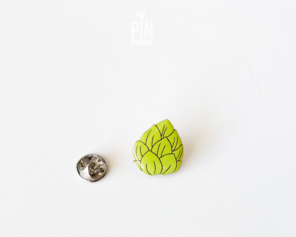 Hand-painted wooden beer hops pin with bright green layered leaves and a glossy finish, shown next to a stainless steel clutch back on a white background.