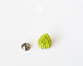 Hand-painted wooden beer hops pin with bright green layered leaves and a glossy finish, shown next to a stainless steel clutch back on a white background.