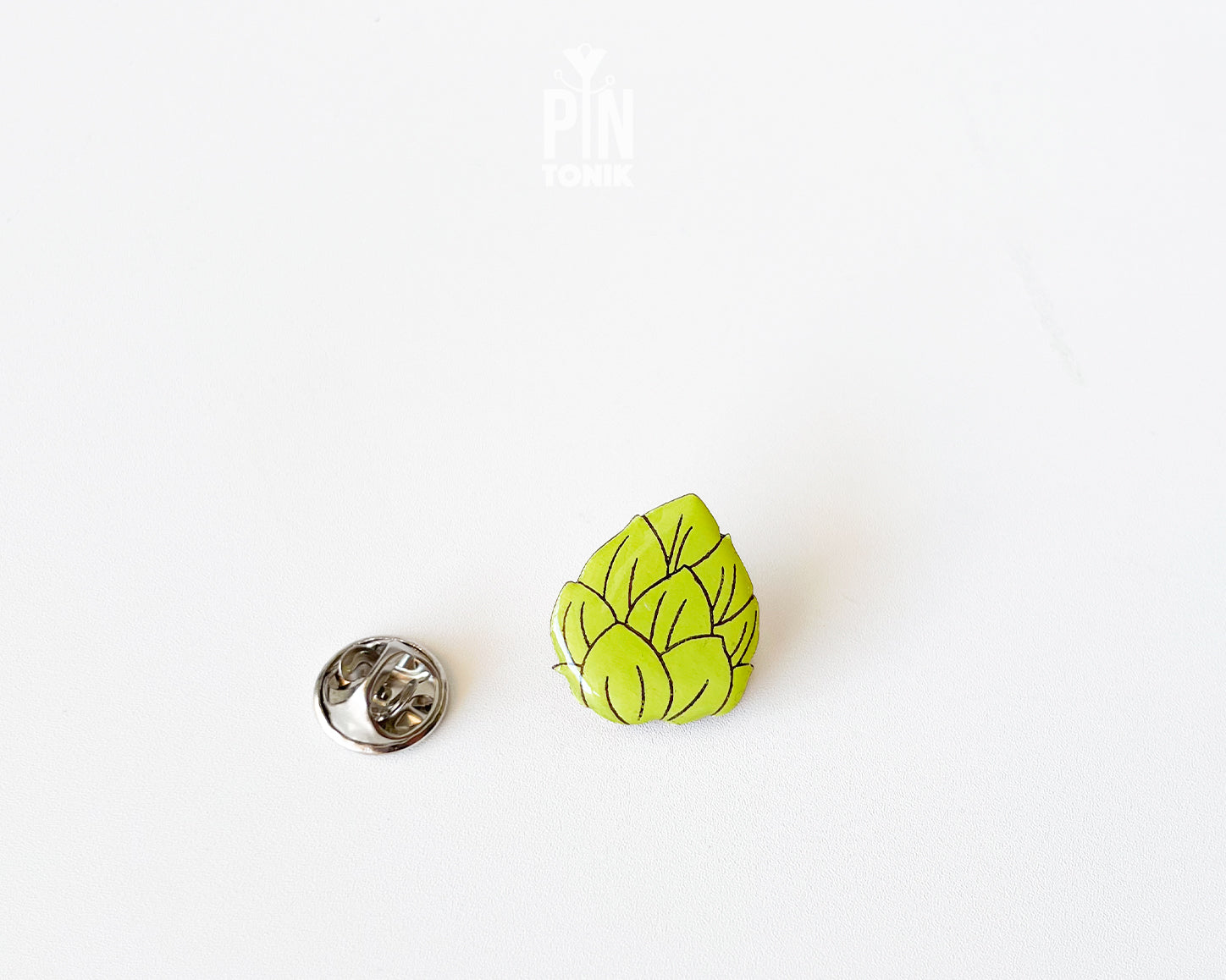 Hand-painted wooden beer hops pin with bright green layered leaves and a glossy finish, shown next to a stainless steel clutch back on a white background.