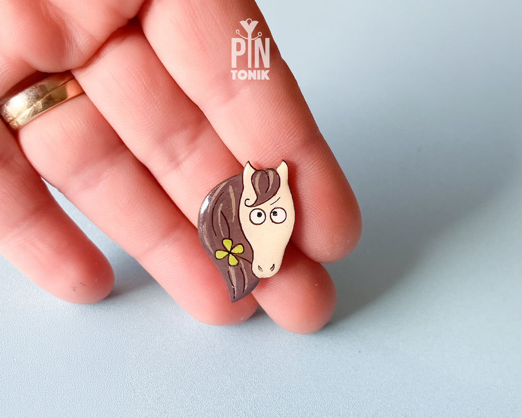 Hand-painted wooden horse pin with a flower in its mane and a funny side-eye expression, finished with glossy resin