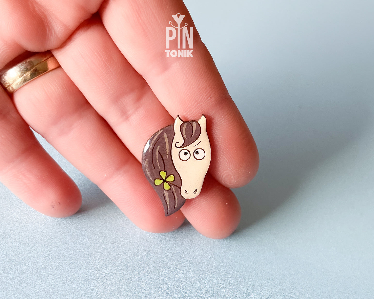 Hand-painted wooden horse pin with a flower in its mane and a funny side-eye expression, finished with glossy resin