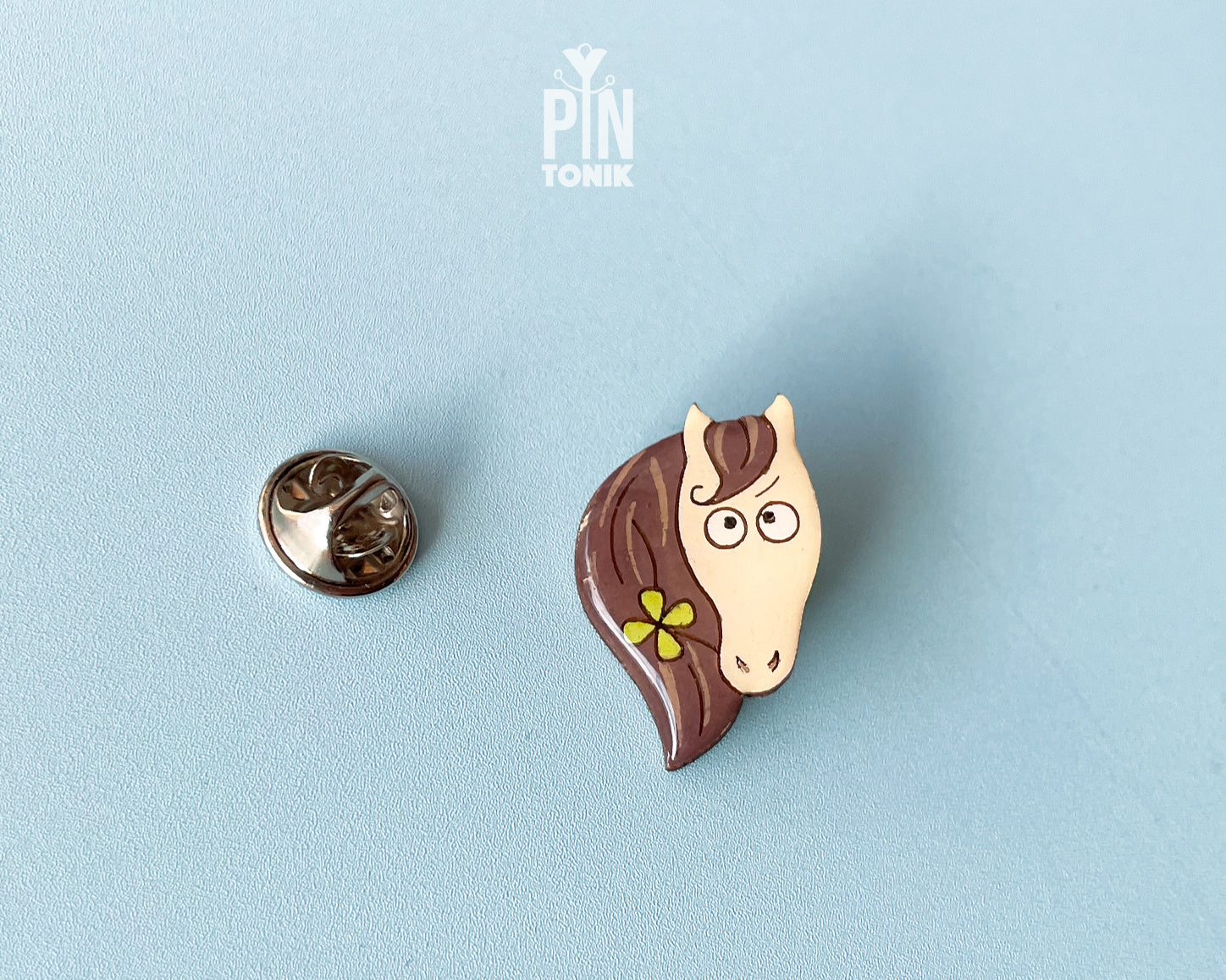 Hand-painted wooden horse pin with a flower in its mane and a funny side-eye expression, finished with glossy resin