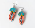 Hand-painted wooden jellyfish dangle earrings with teal caps, coral tentacles, and sterling silver hooks, finished in glossy resin