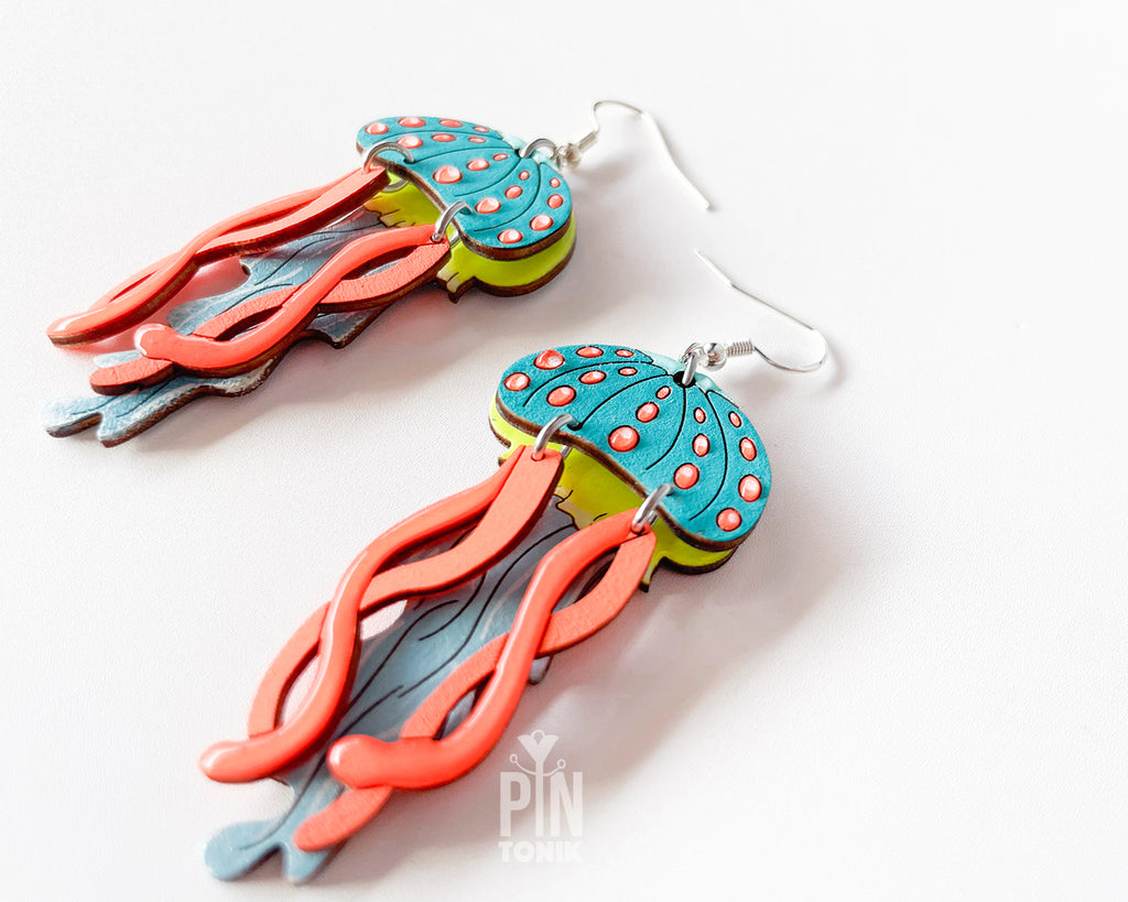 Hand-painted wooden jellyfish dangle earrings with teal caps, coral tentacles, and sterling silver hooks, finished in glossy resin