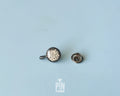 Hand-painted wooden pin shaped like a black frying pan containing a sugar-dusted kaiserschmarrn pancake, shown next to a stainless steel clutch back on a light blue background.