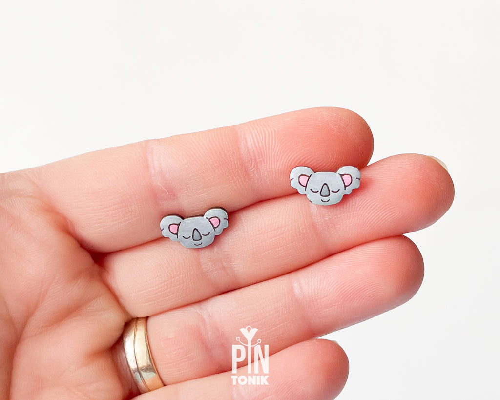 Pair of hand-painted wooden koala stud earrings with pink ears and peaceful closed eyes, finished with glossy resin