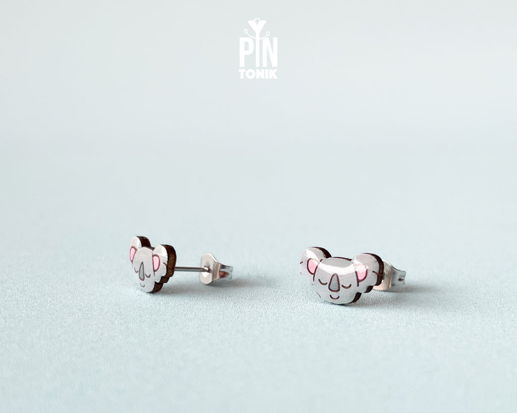 Pair of hand-painted wooden koala stud earrings with pink ears and peaceful closed eyes, finished with glossy resin