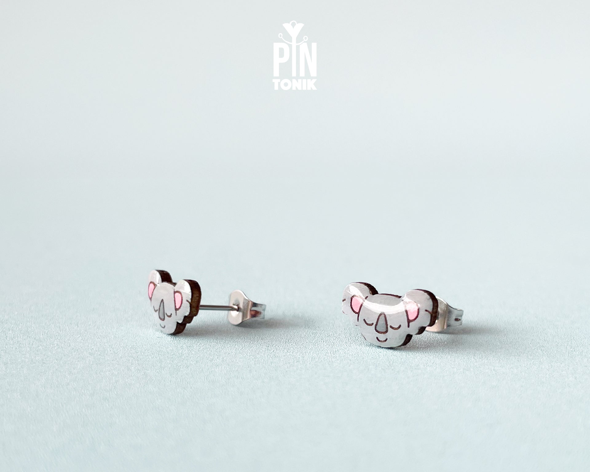 Pair of hand-painted wooden koala stud earrings with pink ears and peaceful closed eyes, finished with glossy resin