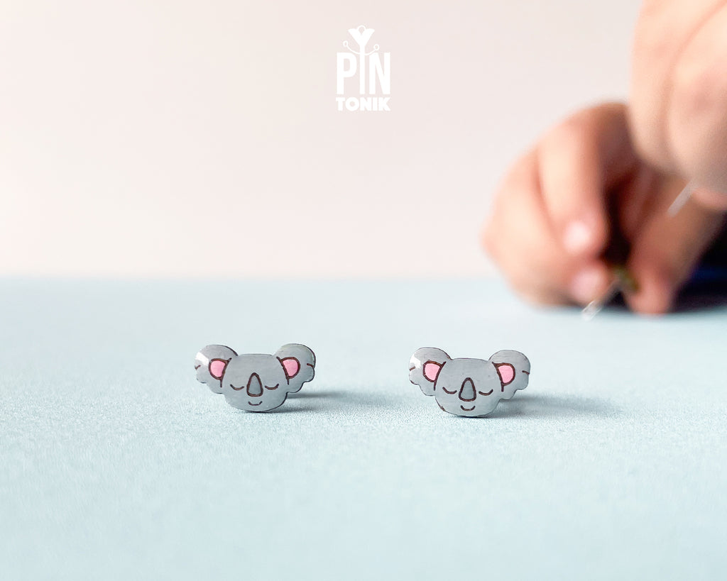 Pair of hand-painted wooden koala stud earrings with pink ears and peaceful closed eyes, finished with glossy resin