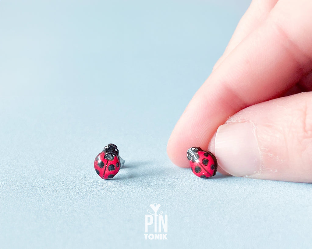 Handmade tiny wooden ladybug stud earrings in classic red and black, measuring a realistic 7-8mm by PinTonik.