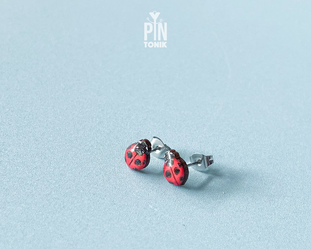 Handmade tiny wooden ladybug stud earrings in classic red and black, measuring a realistic 7-8mm by PinTonik.