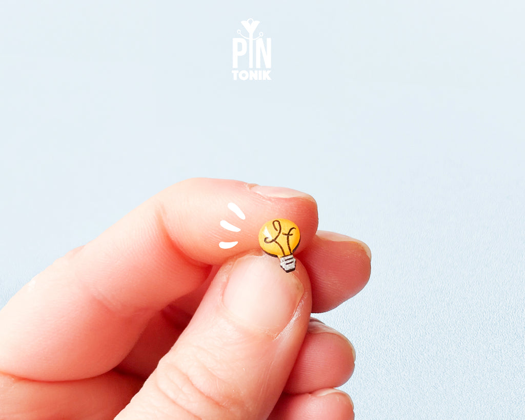 Handmade wooden bright yellow lightbulb stud earrings with a detailed grey metallic base illustration by PinTonik.