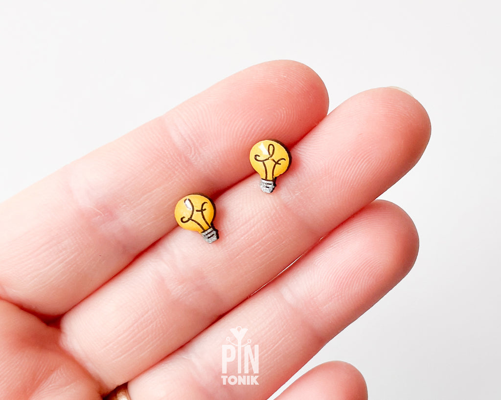 Handmade wooden bright yellow lightbulb stud earrings with a detailed grey metallic base illustration by PinTonik.