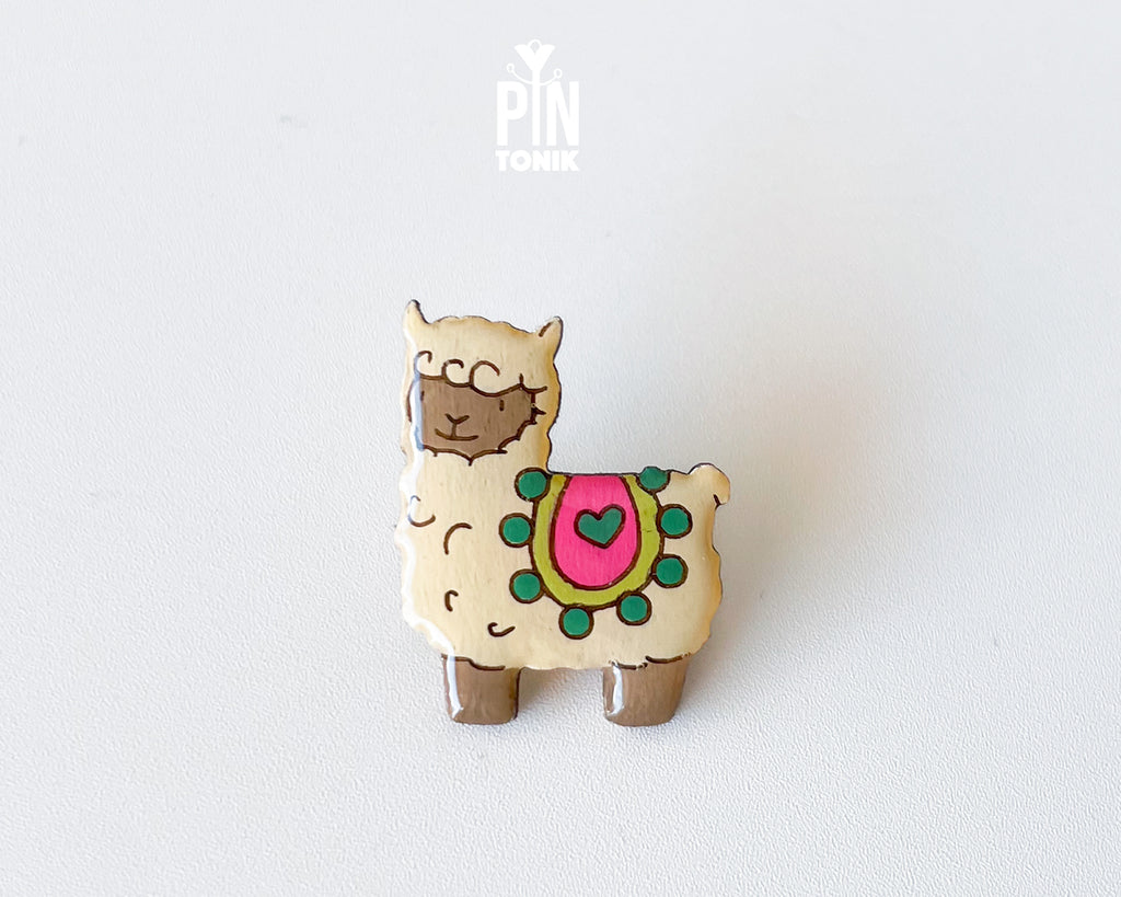 Hand-painted wooden llama pin with a colorful saddle and heart detail, finished with glossy resin