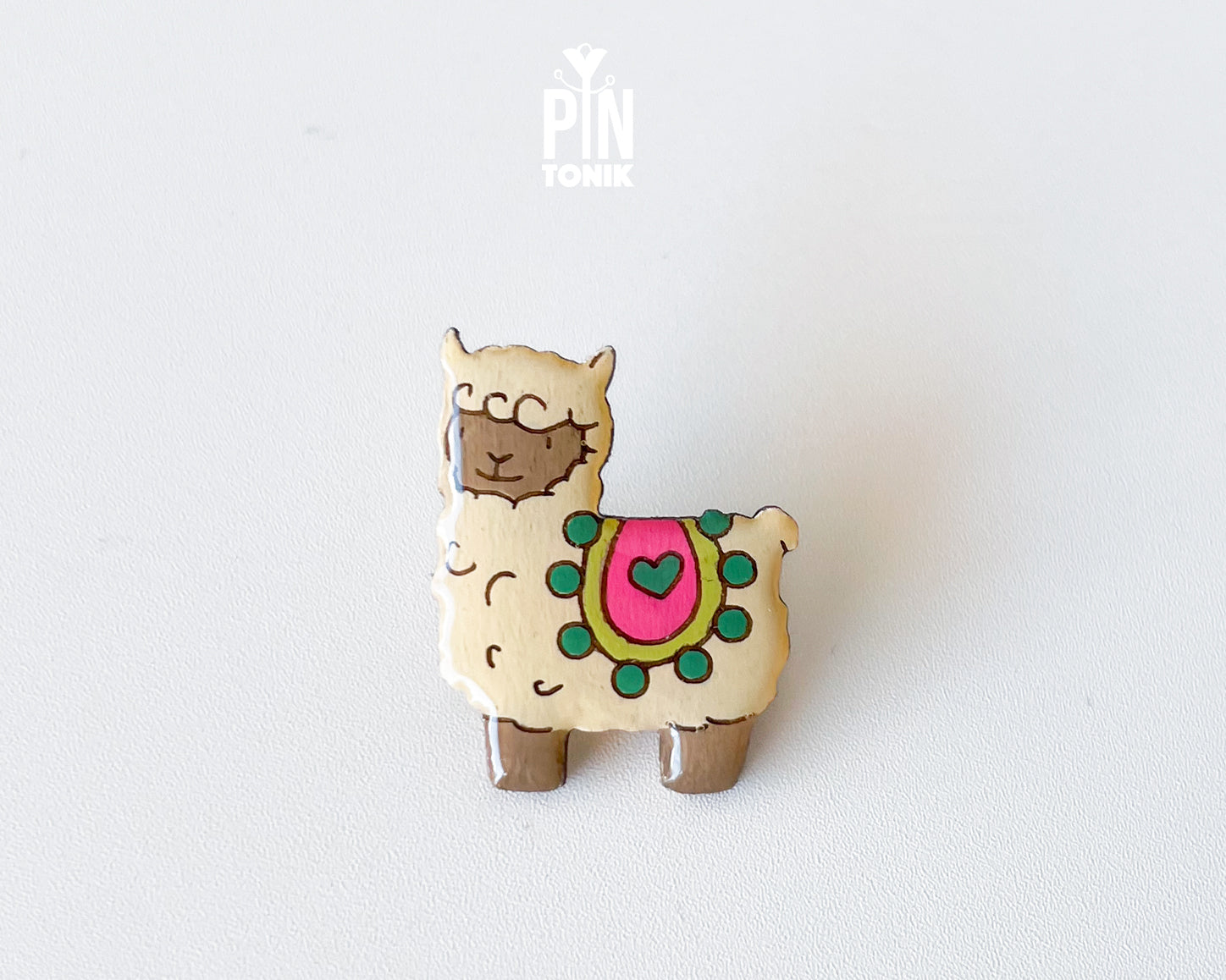 Hand-painted wooden llama pin with a colorful saddle and heart detail, finished with glossy resin