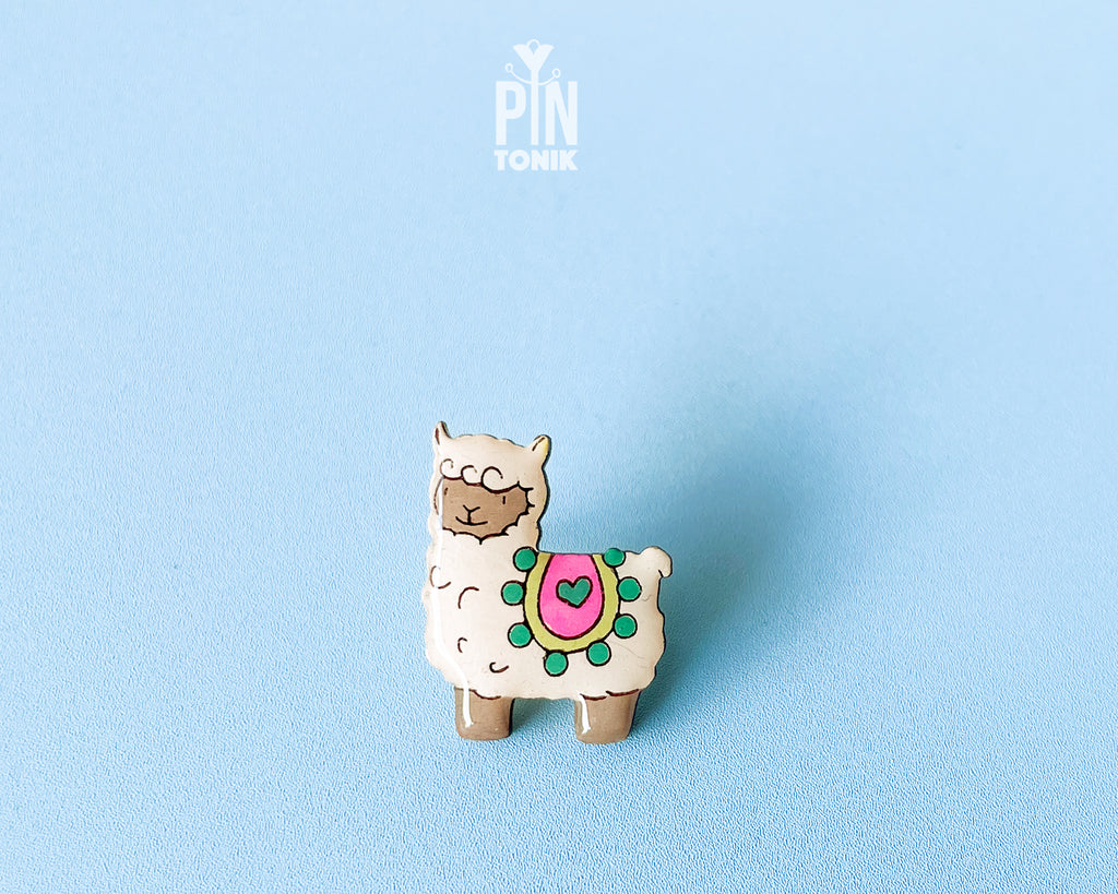 Hand-painted wooden llama pin with a colorful saddle and heart detail, finished with glossy resin