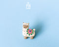 Hand-painted wooden llama pin with a colorful saddle and heart detail, finished with glossy resin