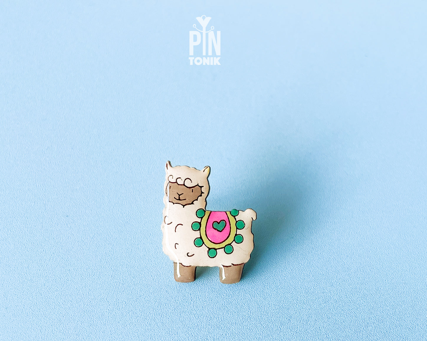 Hand-painted wooden llama pin with a colorful saddle and heart detail, finished with glossy resin